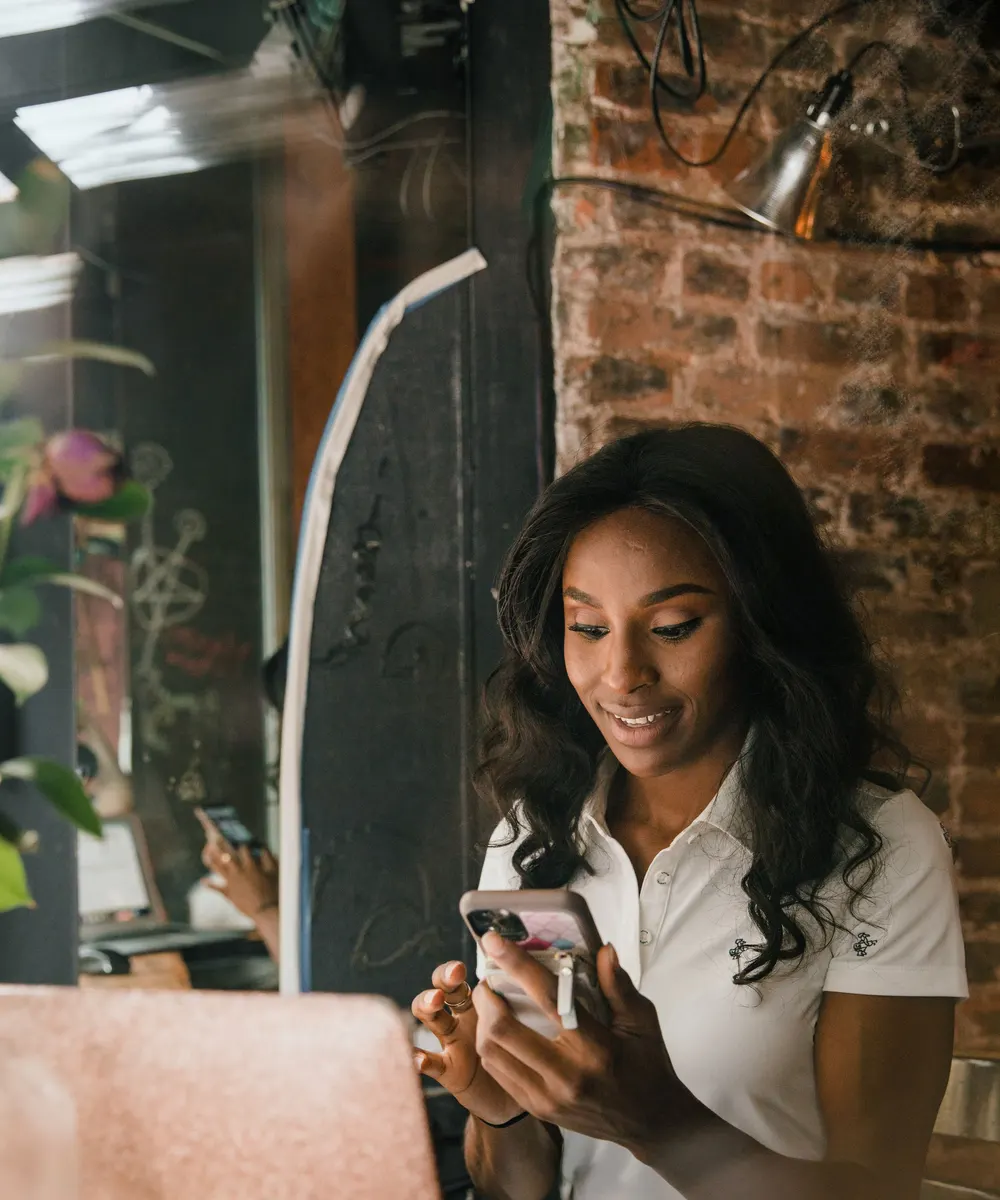 Dona de um pequeno negócio sorrindo enquanto usa o celular no balcão da loja